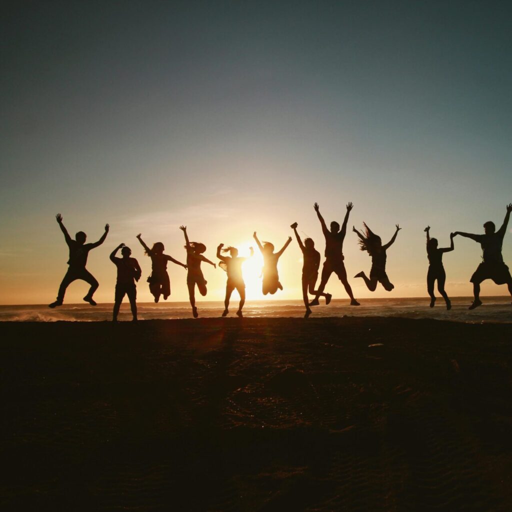 Silhouette of a group of friends jumping on a beach at sunset, expressing joy and freedom.