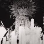 A serene black and white image of a religious statue surrounded by candles in Carmona, Spain.