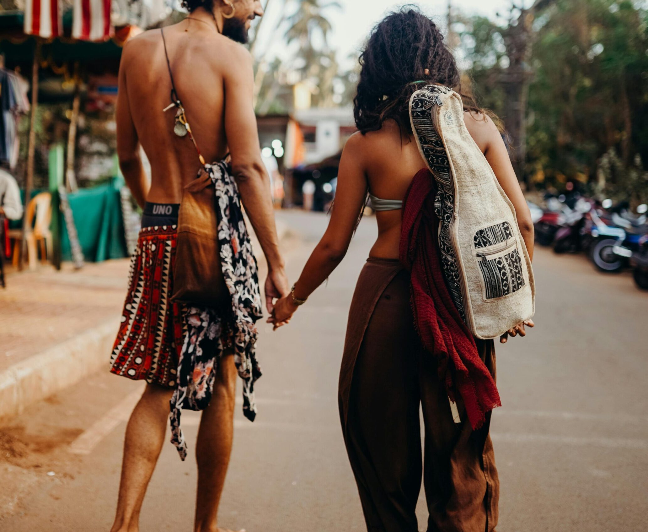 A romantic couple holding hands while walking down an outdoor market street on a sunny day.