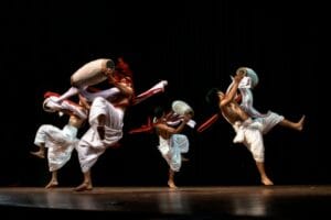Dynamic group of dancers performing a traditional dance with drums on stage.